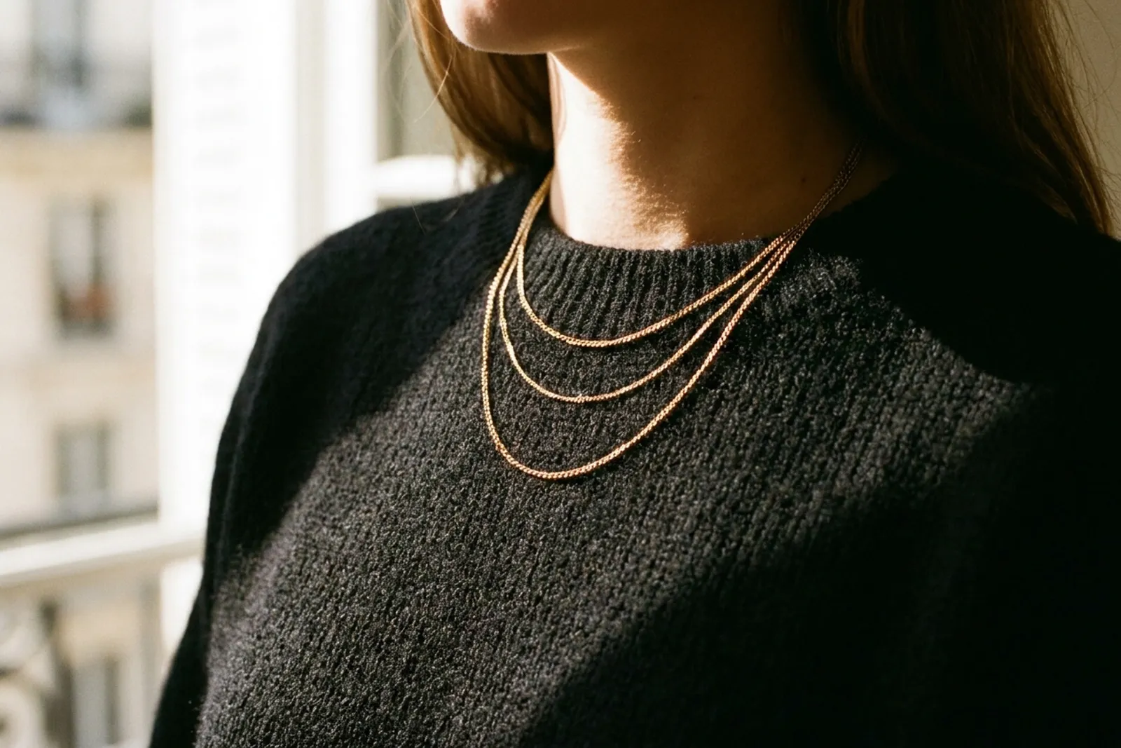 Gros plan sur un décolleté avec trois chaînes dorées superposées portées sur une maille noire